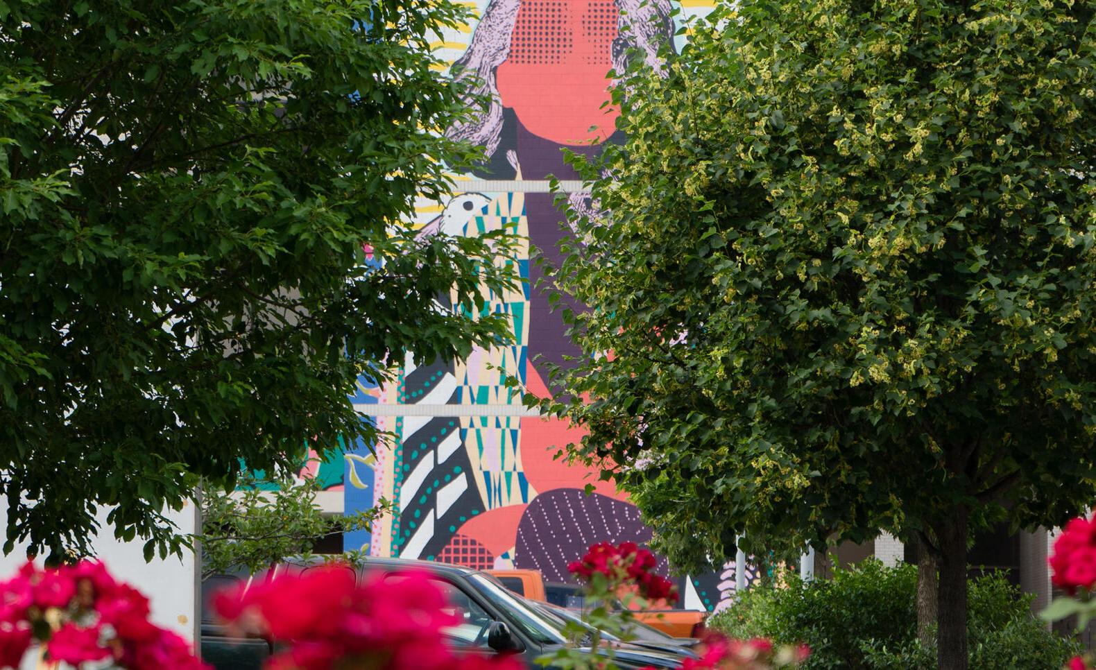 FAILE mural peeking through trees and flowers