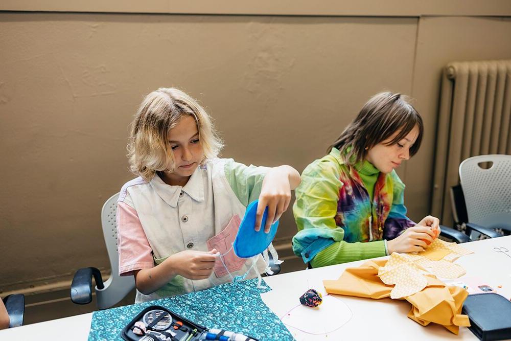 Two students sit at a table working with brightly colored felt. 